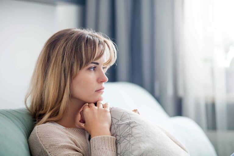 Thoughtful woman sitting on couch in living room with natural light.